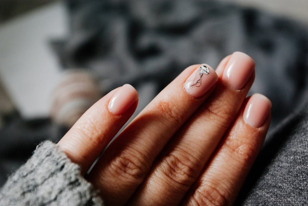 From above of crop unrecognizable female in warm sweater demonstrating hands with manicure with creative nail art
